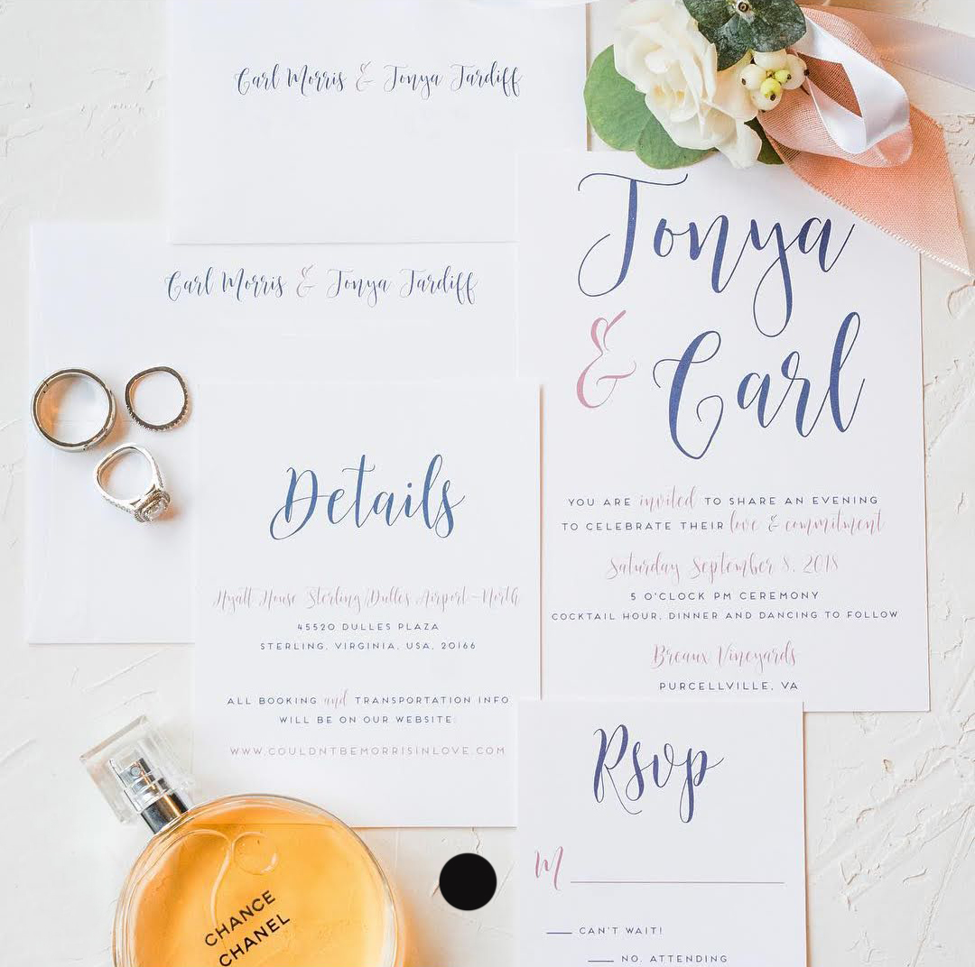 A wedding invitation suite laid out with wedding rings, a bouquet, and perfume.